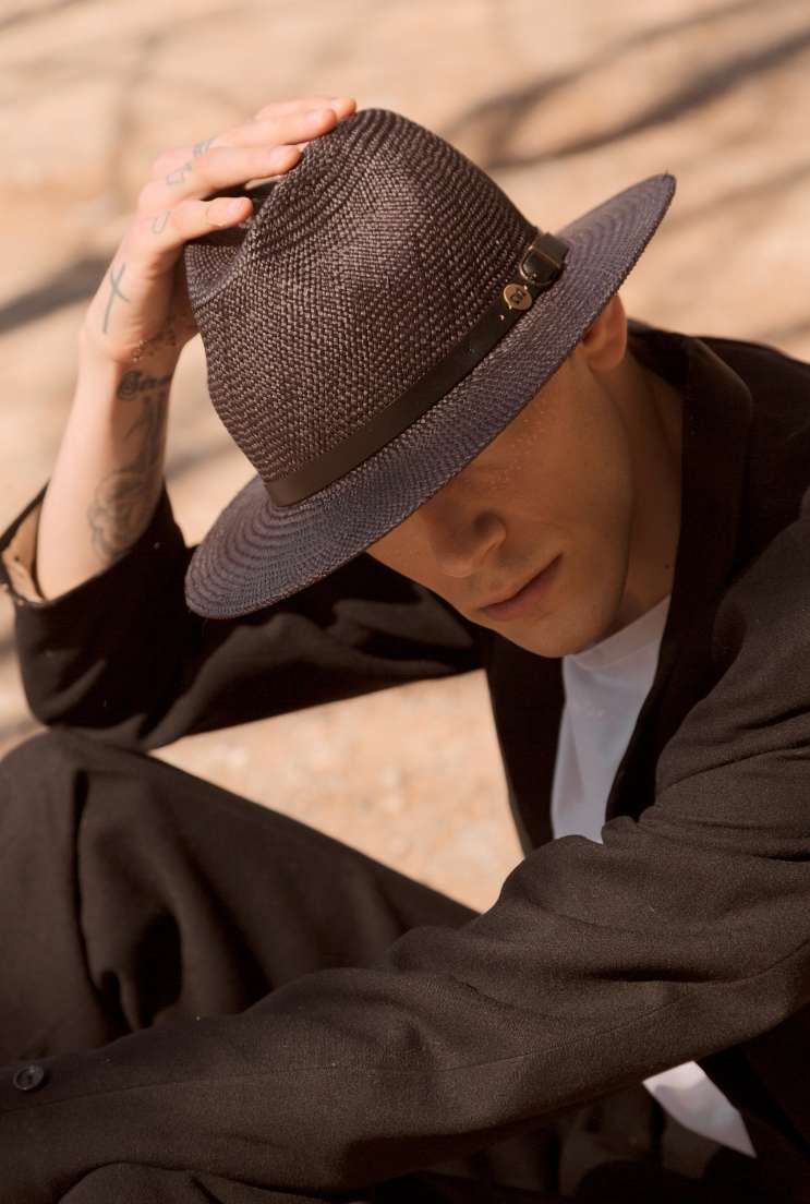 foto di un ragazzo giovane vestito di nero con sguardo coperto da un cappello nero in paglia panama di primario nesti