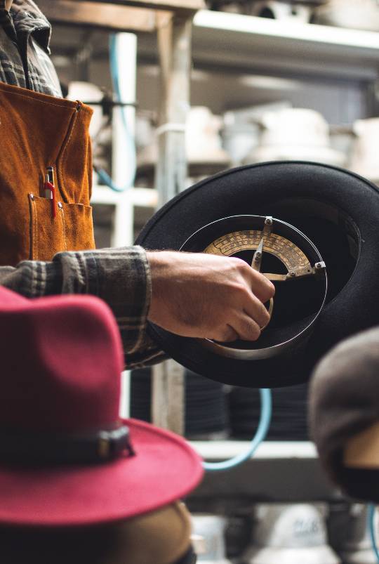 foto ravvicinata di Simone di Primario Nesti che misura la circonferenza di un cappello usando un misuratore vecchio stile
