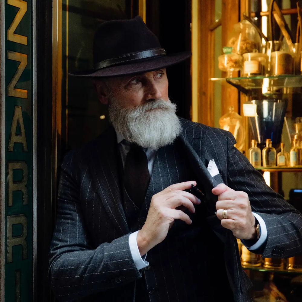 modello adulto con barba bianca indossa un cappello fedora tradizionale primario nesti antipioggia colore marrone in un atmosfera boutique