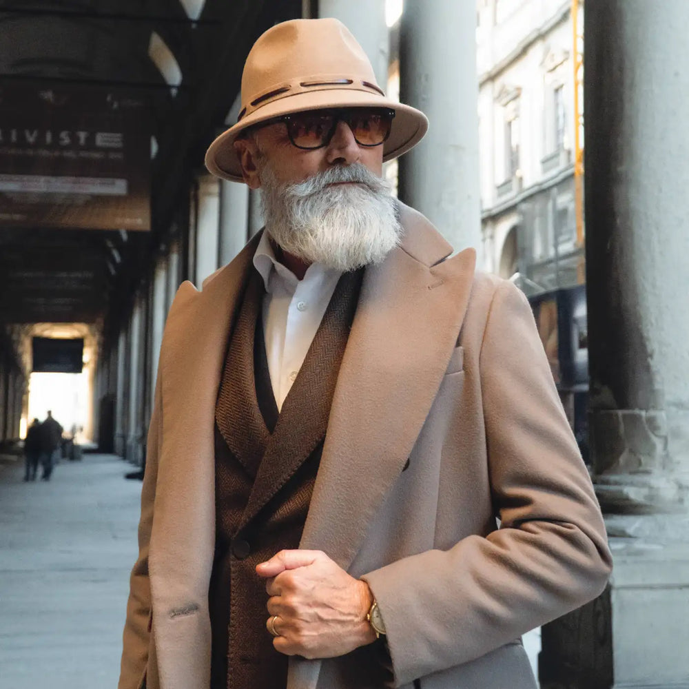 modello maturo con cappello fedora tesa corta primario nesti antipioggia colore beige nel suo outfit formale beige scuro con sfondo di portici fiorentin