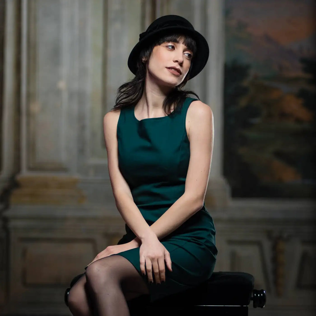 cappello a cloche in feltro di lana merinos con nastro di velluto primario nesti nero modella seduta su panchetto storico atmosfera retro contemporanea