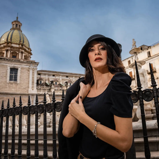 modella adulta con look total black e cappello a cloche signorile a tesa media primario nesti con sfondo cattedrale e cancellata antica