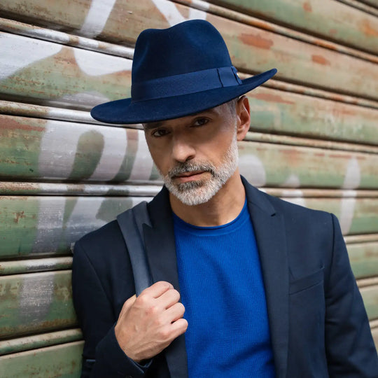 modello adulto con barba indossa un cappello fedora in feltro di morbido cashmere primario nesti navy nel suo look contemporaneo su sfondo street art