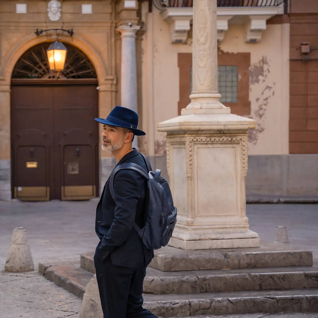 modello adulto con cappello fedora in feltro di morbido cashmere blu primario nesti nel cortile di un palazzo storico siciliano