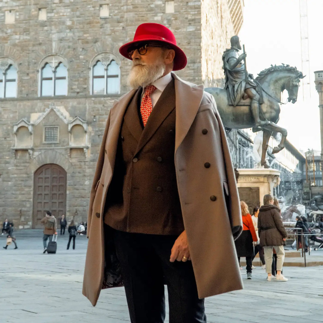 modello elegante con cappello indiana jones primario nesti in lana merinos rosso indossa un cappotto cammello con lo sfondo di palazzo vecchio in stile toscano autentico