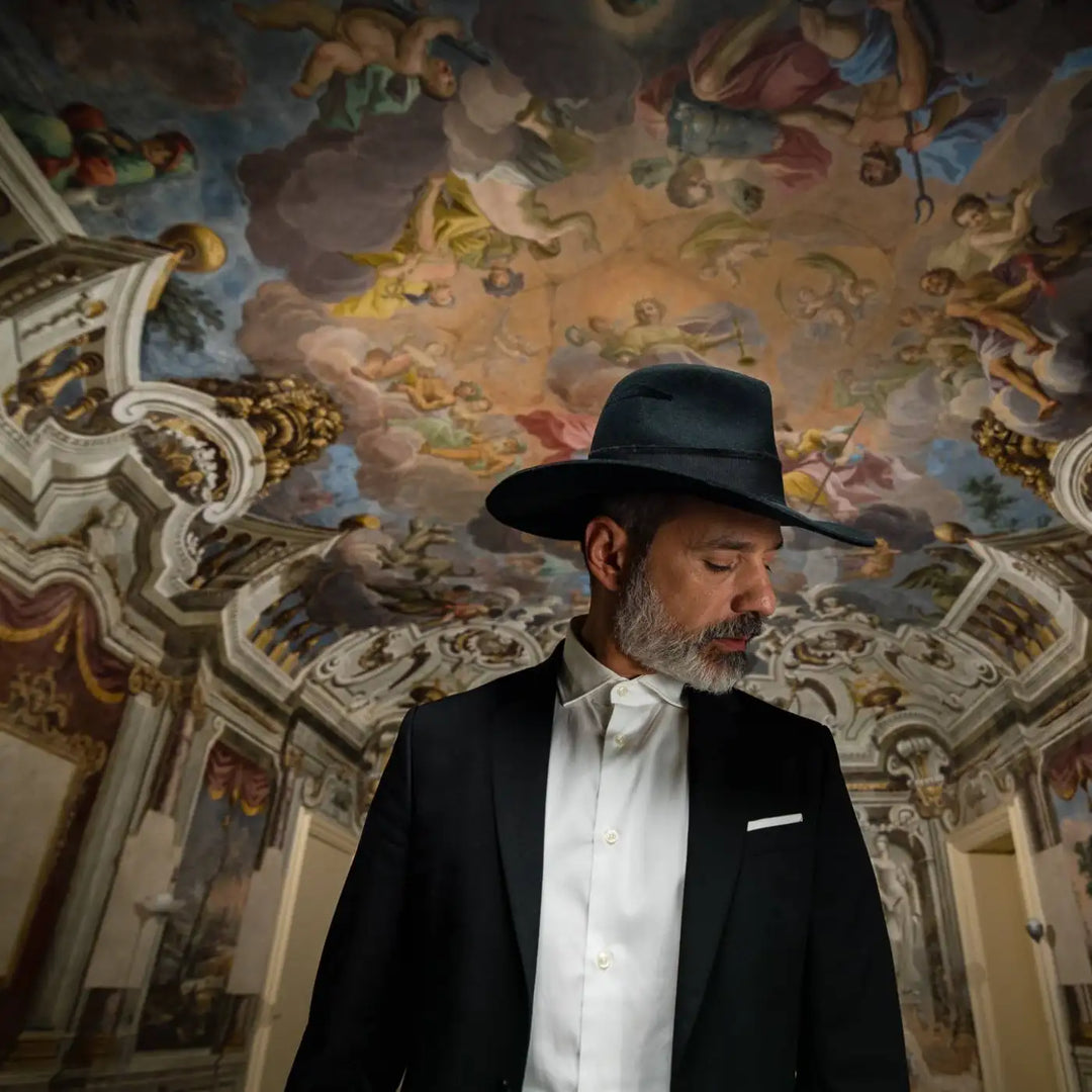 modello maturo con barba bianca indossa cappello fedora a tesa larga piatta in feltro di lana merinos nero su sfondo architettonico