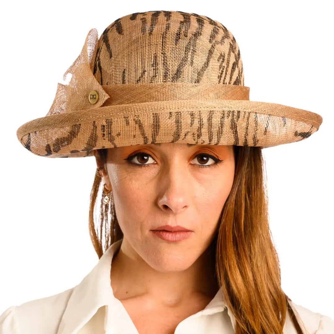 primo piano frontale di donna con capelli lunghi che indossa un cappello da cerimonia estivo con fiocco color camel animalier fatto da cappelleria primario nesti