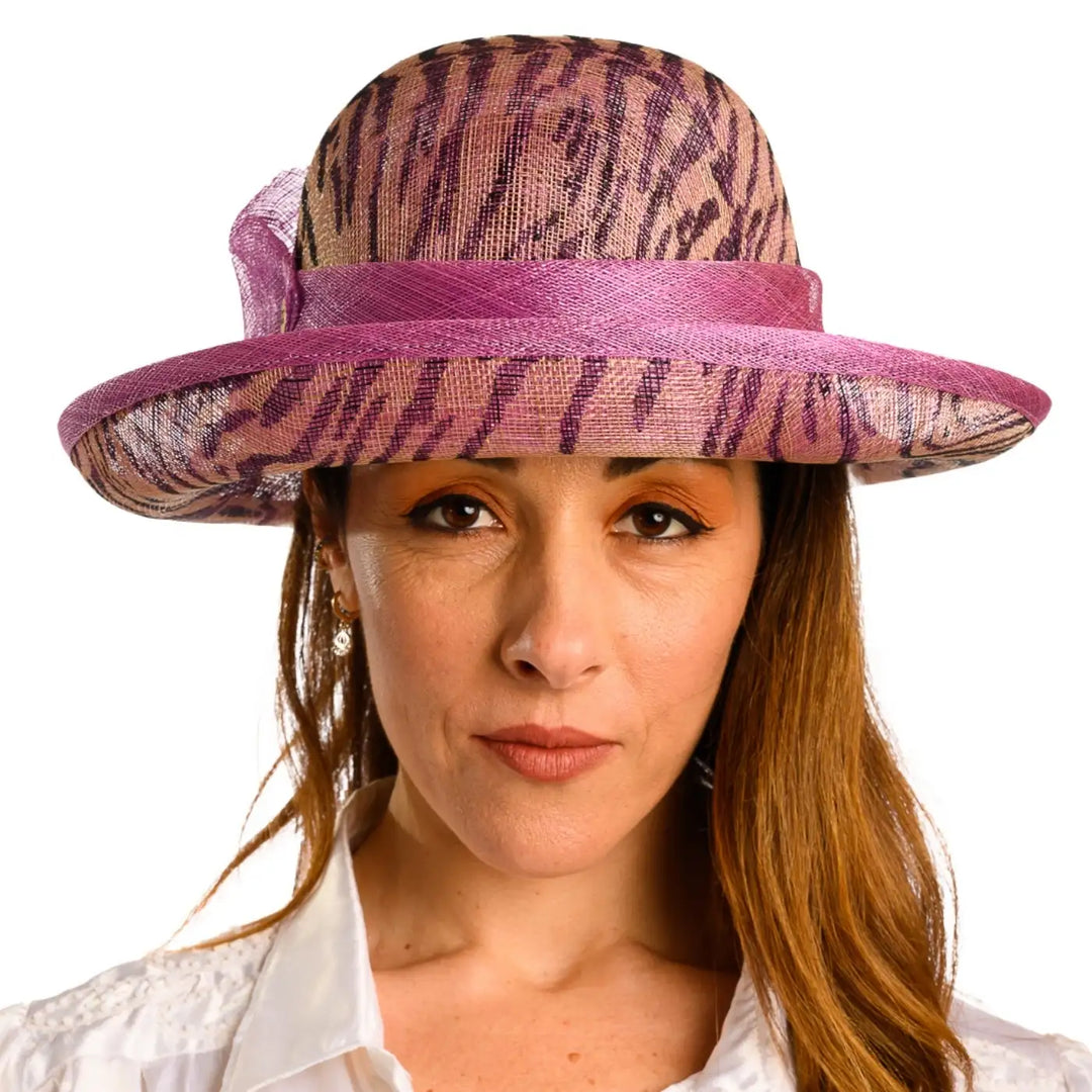primo piano frontale di donna con capelli lunghi che indossa un cappello da cerimonia estivo con fiocco color ciclamino animalier fatto da primario nesti