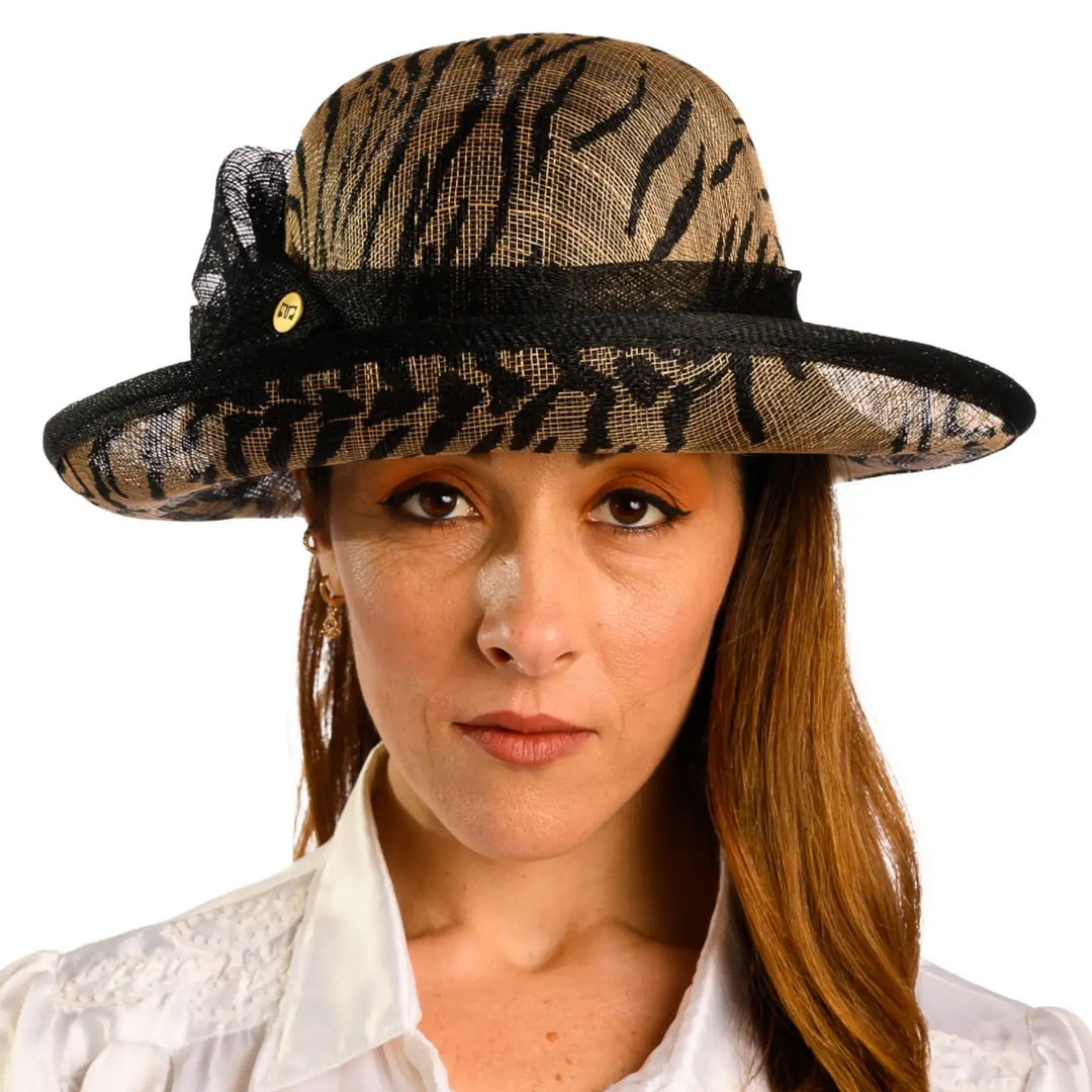 primo piano frontale di donna con capelli lunghi che indossa un cappello da cerimonia estivo con fiocco color nero animalier fatto da cappelleria primario nesti