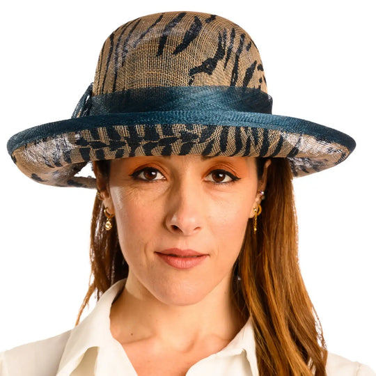 primo piano frontale di donna con capelli lunghi che indossa un cappello da cerimonia estivo con fiocco color petrolio animalier fatto da primario nesti