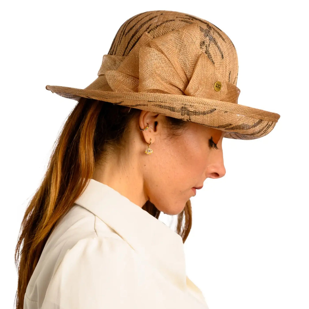 primo piano laterale di donna adulta con capelli lunghi che indossa un cappello da cerimonia estivo con fiocco color camel animalier realizzato da primario nesti