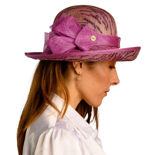 primo piano laterale di donna adulta con capelli lunghi che indossa un cappello da cerimonia estivo con fiocco color ciclamino animalier realizzato da primario nesti