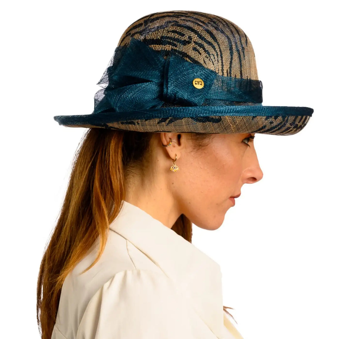primo piano laterale di donna adulta con capelli lunghi che indossa un cappello da cerimonia estivo con fiocco color petrolio animalier realizzato da primario nesti