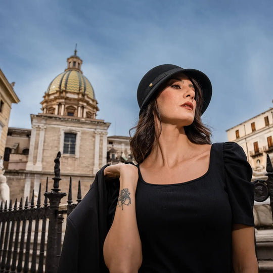 profilo di modella adulta con cappello a cloche signorile a tesa media primario nesti con sfondo di cupola barocca e outfit total black