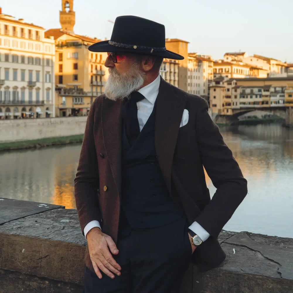 profilo di modello raffinato con cappello australiano primario nesti di lana merinos marrone nel suo outfit formale con sfondo ponte vecchio e riflessi dorati al tramonto