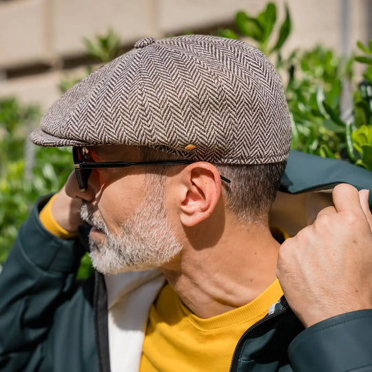 profilo lateraledi uomo maturo con coppola peaky blinders primario nesti invernale maglione giallo e barba grigia