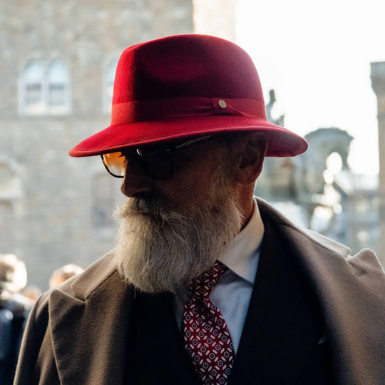 profilo ravvicinato di modello con barba curata e cappello indiana jones primario nesti rosso in lana merinos a tono con la cravatta per un look raffinato italiano