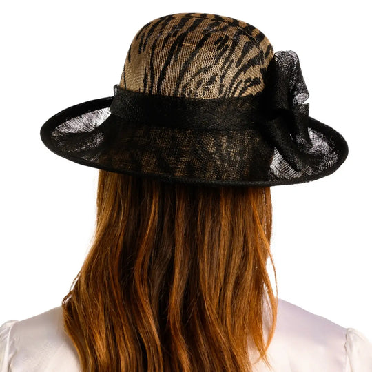 vista posteriore di una donna con capelli lunghi che indossa un cappello da cerimonia estivo con fiocco color nero animalier fatto a mano da primario nesti