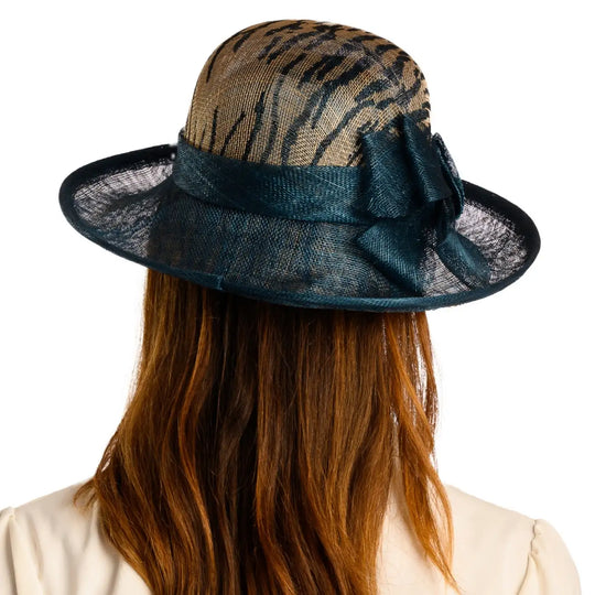 vista posteriore di una donna con capelli lunghi che indossa un cappello da cerimonia estivo con fiocco color petrolio animalier fatto a mano da primario nesti